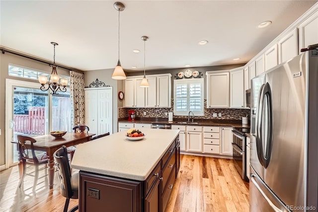 kitchen with stainless steel appliances, a sink, white cabinetry, backsplash, and light wood finished floors