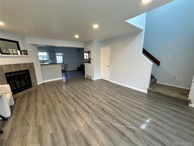 unfurnished living room featuring wood finished floors, visible vents, baseboards, stairway, and a tiled fireplace