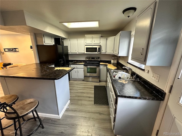 kitchen with dark countertops, appliances with stainless steel finishes, a sink, light wood-type flooring, and a peninsula