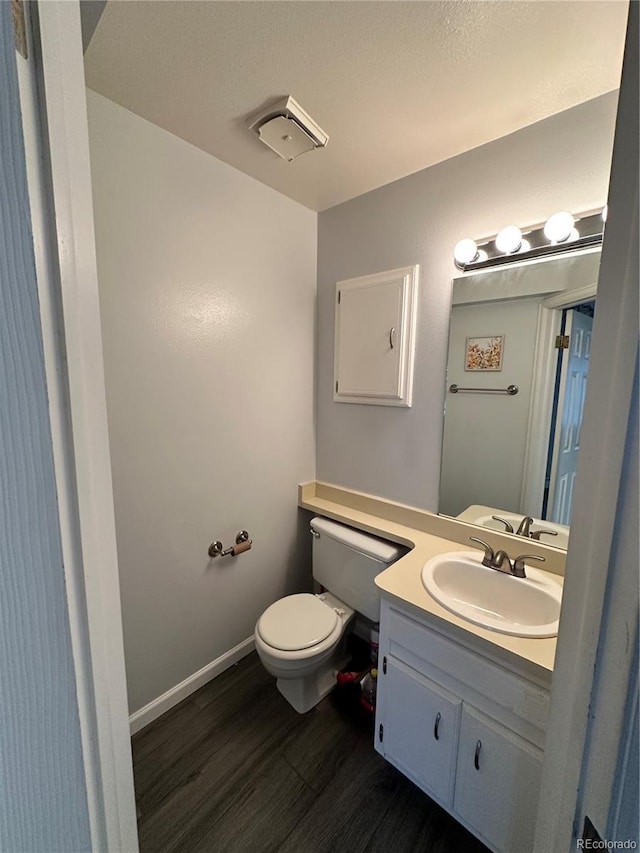 half bath with vanity, wood finished floors, toilet, and baseboards