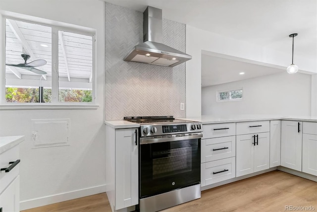 kitchen with stainless steel stove, hanging light fixtures, wall chimney exhaust hood, and plenty of natural light