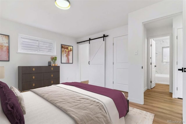 bedroom with light wood-type flooring, ensuite bath, and a barn door