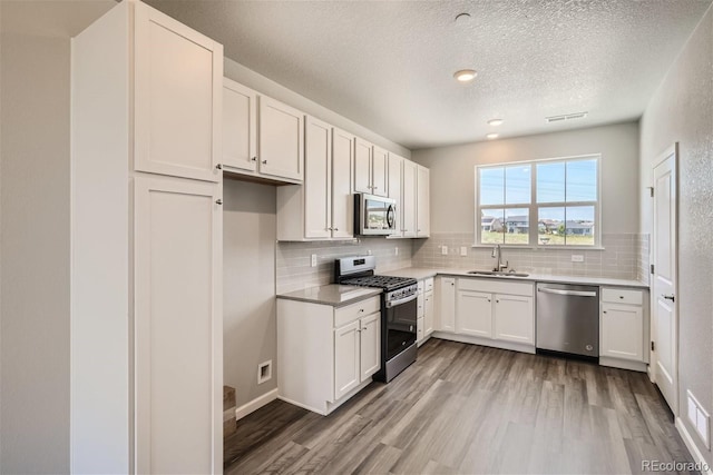 kitchen featuring white cabinets, sink, light hardwood / wood-style flooring, a textured ceiling, and appliances with stainless steel finishes