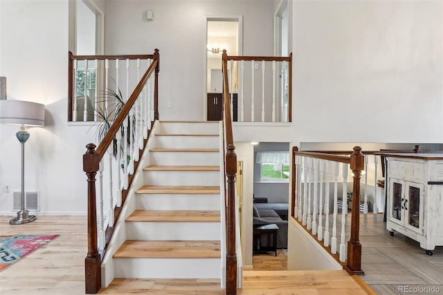 stairway with wood finished floors and a towering ceiling