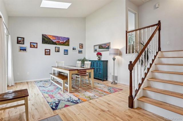 dining area featuring a skylight, high vaulted ceiling, wood finished floors, stairway, and baseboards