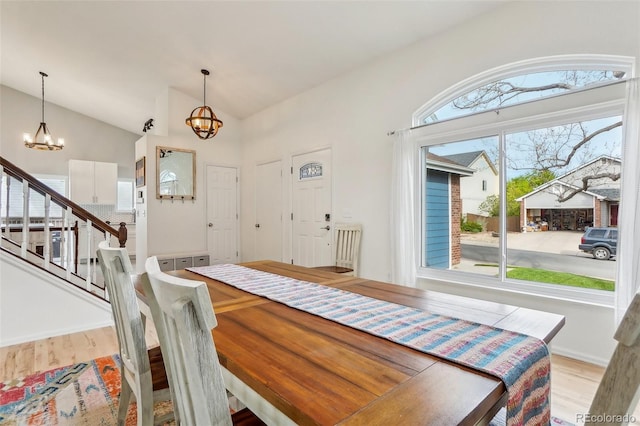 dining area featuring a chandelier, wood finished floors, lofted ceiling, and stairs