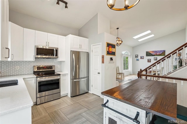 kitchen featuring stainless steel appliances, white cabinetry, backsplash, decorative light fixtures, and a skylight