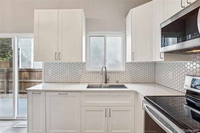 kitchen featuring stainless steel appliances, a sink, white cabinets, light countertops, and tasteful backsplash