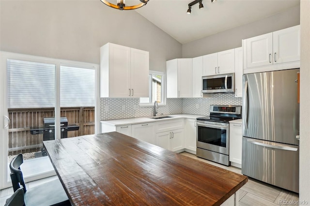 kitchen with stainless steel appliances, a sink, decorative backsplash, white cabinetry, and lofted ceiling