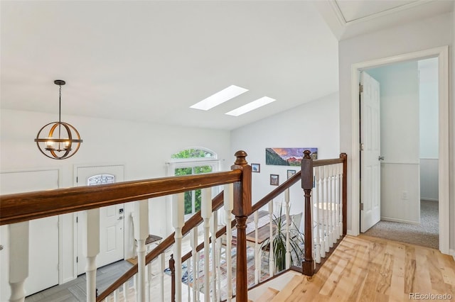 hallway with a skylight, an upstairs landing, light wood-type flooring, lofted ceiling, and a chandelier