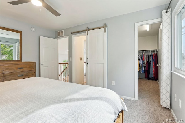carpeted bedroom featuring a spacious closet, baseboards, a barn door, a closet, and ceiling fan