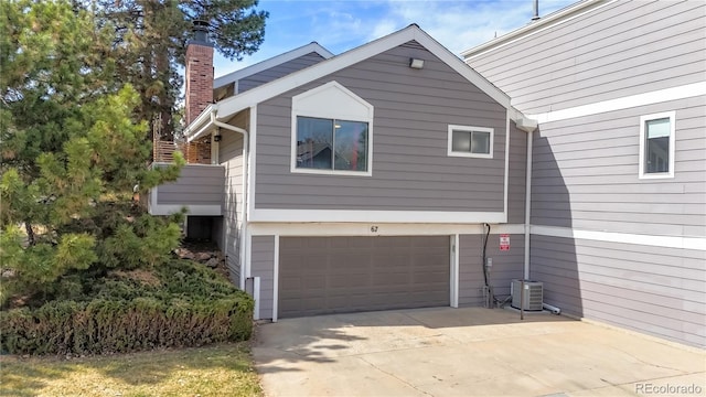 view of side of home featuring cooling unit, driveway, a chimney, and an attached garage