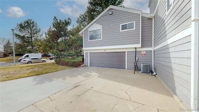 view of home's exterior with driveway, central AC, and a garage