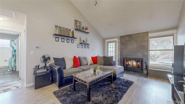 living area with baseboards, high vaulted ceiling, wood finished floors, and a tiled fireplace