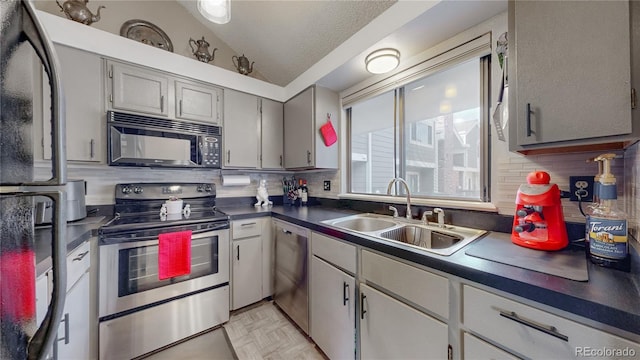 kitchen featuring dark countertops, lofted ceiling, decorative backsplash, stainless steel appliances, and a sink