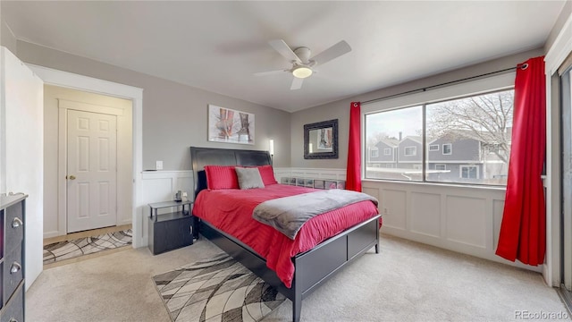 bedroom featuring light carpet, wainscoting, a ceiling fan, and a decorative wall