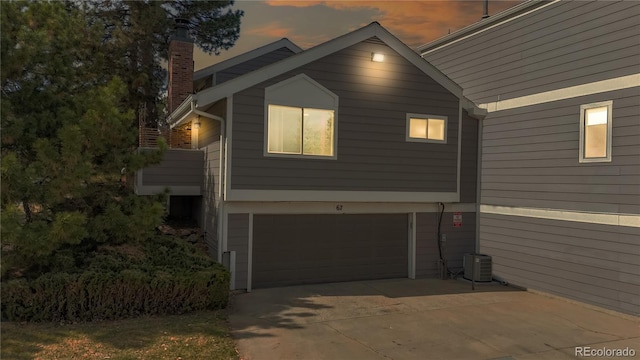 property exterior at dusk featuring a chimney, concrete driveway, central AC, and a garage