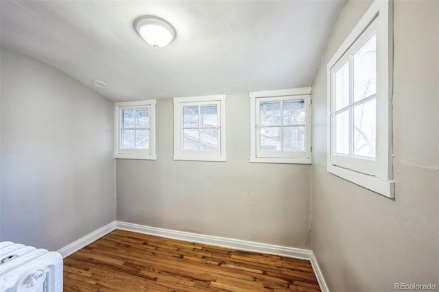 empty room with hardwood / wood-style floors, vaulted ceiling, and radiator heating unit