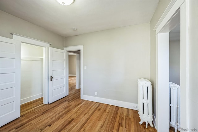 unfurnished bedroom with a closet, radiator heating unit, and wood-type flooring