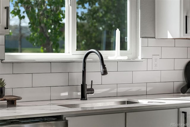 details featuring light stone countertops, dishwasher, a sink, white cabinets, and tasteful backsplash