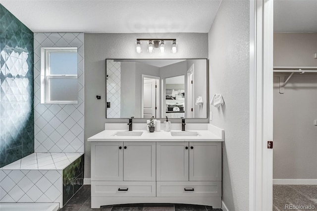 bathroom with a walk in closet, double vanity, a sink, and a textured wall