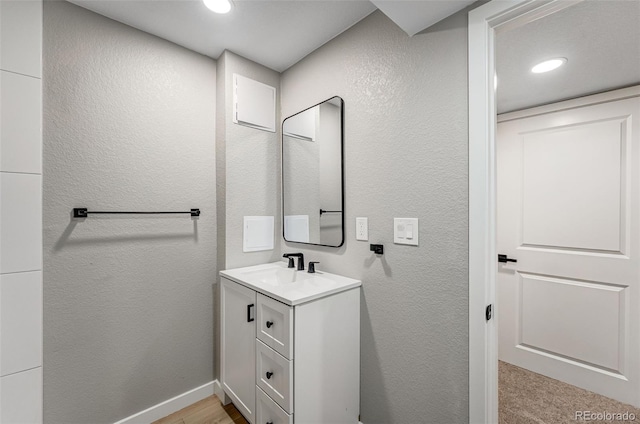 bathroom with baseboards, vanity, recessed lighting, and a textured wall