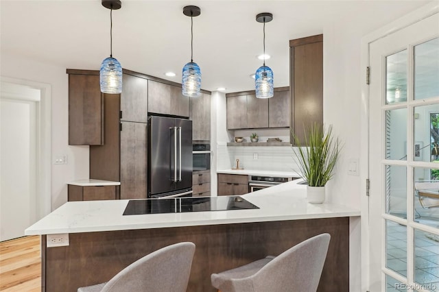 kitchen featuring appliances with stainless steel finishes, a peninsula, light countertops, open shelves, and a kitchen bar