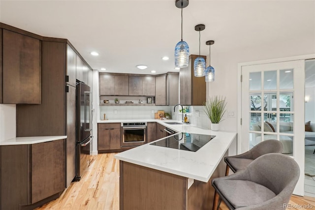 kitchen featuring appliances with stainless steel finishes, a peninsula, a sink, tasteful backsplash, and light wood-style flooring