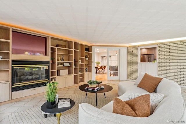 living area with light tile patterned floors, built in shelves, a glass covered fireplace, and brick wall