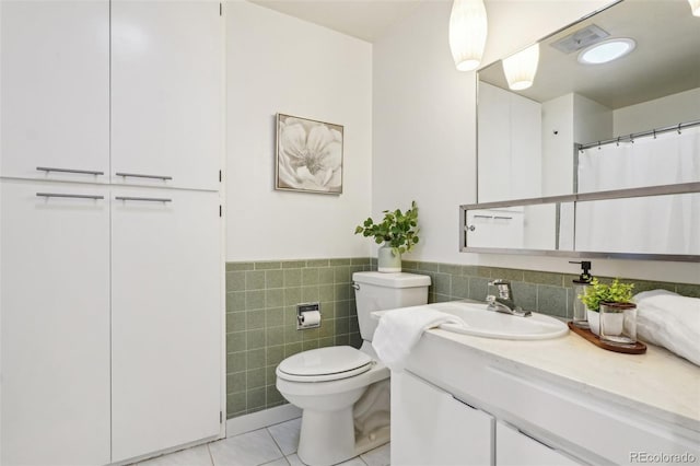 full bath featuring toilet, vanity, tile walls, tile patterned flooring, and a wainscoted wall