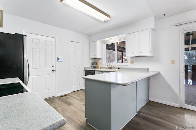 kitchen featuring kitchen peninsula, wood-type flooring, sink, white cabinetry, and stainless steel refrigerator