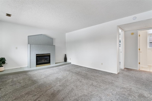 unfurnished living room with a tiled fireplace, a textured ceiling, and carpet