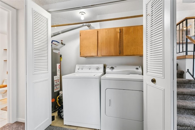 washroom featuring light tile patterned floors, cabinets, water heater, and washer and clothes dryer