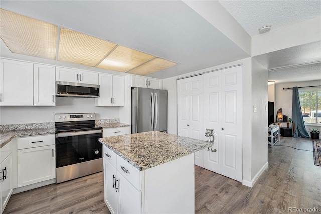 8666 Mariposa St, Thornton, CO 80260 - kitchen with a center island, wood finished floors, white cabinets, appliances with stainless steel finishes, and light stone counters