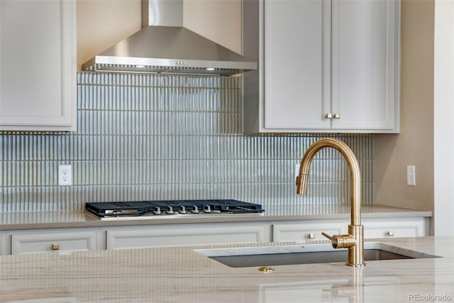 kitchen featuring white cabinetry, sink, light stone counters, and wall chimney exhaust hood