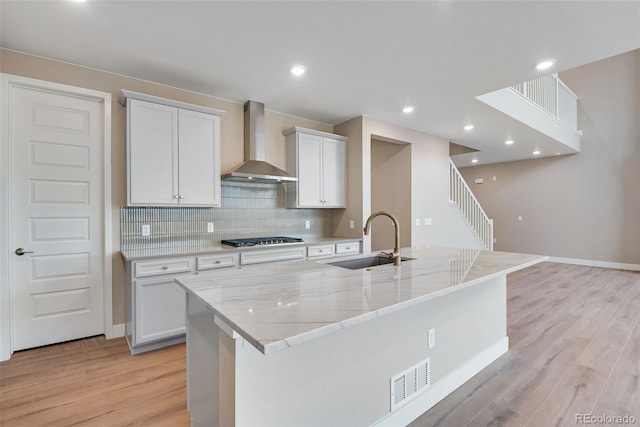 kitchen with a large island, sink, stainless steel gas cooktop, white cabinets, and wall chimney exhaust hood