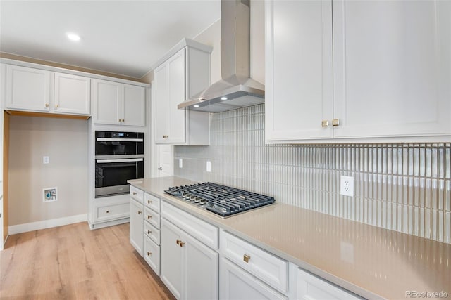 kitchen with stainless steel gas cooktop, double wall oven, wall chimney range hood, decorative backsplash, and white cabinets