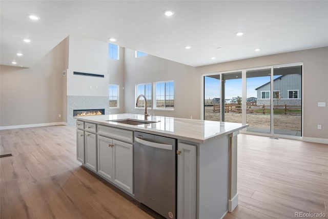 kitchen featuring sink, a center island with sink, light wood-type flooring, stainless steel dishwasher, and light stone countertops