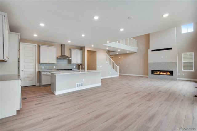 kitchen featuring a center island with sink, wall chimney range hood, white cabinets, and light hardwood / wood-style floors