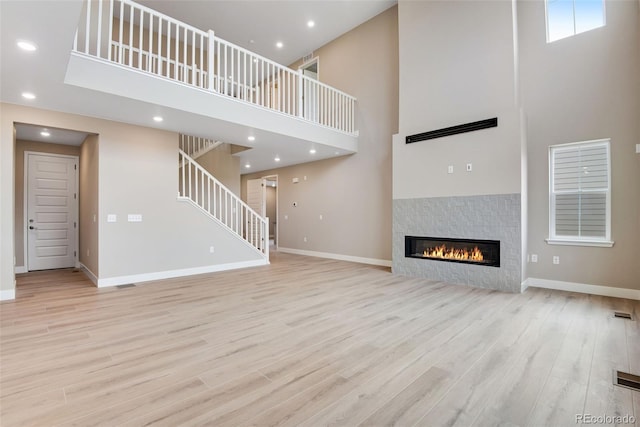 unfurnished living room with a fireplace, a towering ceiling, and light hardwood / wood-style flooring