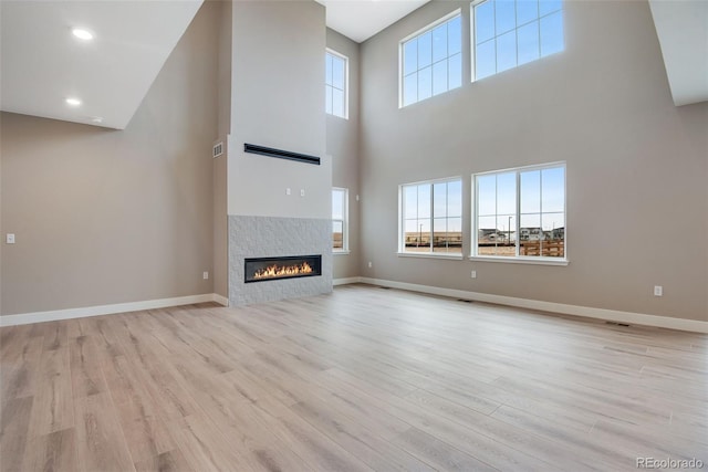 unfurnished living room with a tiled fireplace, a towering ceiling, and light wood-type flooring