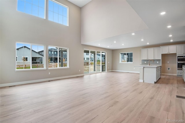 unfurnished living room with sink, a towering ceiling, and light wood-type flooring