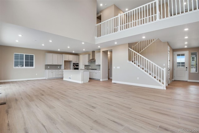 unfurnished living room featuring sink, light wood-type flooring, and a high ceiling