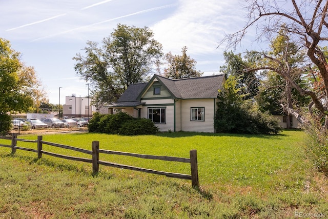 view of front facade featuring a shingled roof, a front yard, and fence