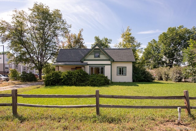 view of front of house featuring a shingled roof, a front yard, and fence