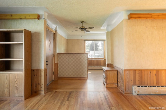 hall with a wainscoted wall, a baseboard radiator, wooden walls, a textured ceiling, and wood finished floors