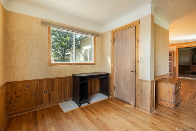 spare room with a wainscoted wall, wood walls, a textured ceiling, and wood finished floors