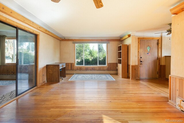 unfurnished living room featuring a wealth of natural light, a ceiling fan, wood finished floors, and wainscoting