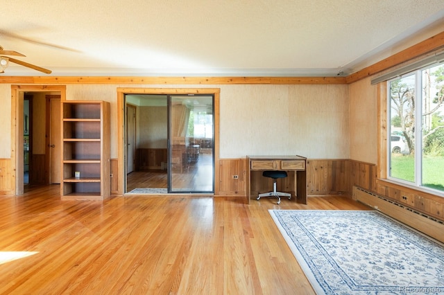 unfurnished office featuring ceiling fan, a baseboard radiator, wooden walls, wood finished floors, and wainscoting