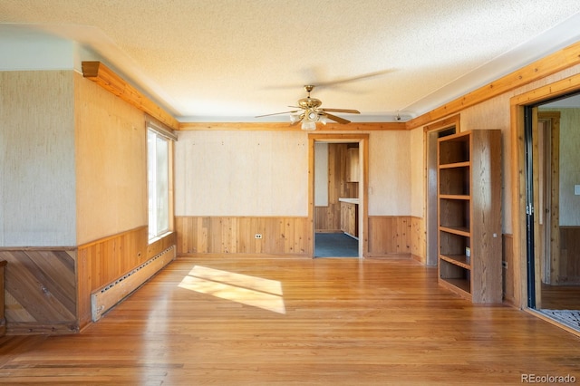 spare room with a wainscoted wall, baseboard heating, a textured ceiling, and wooden walls